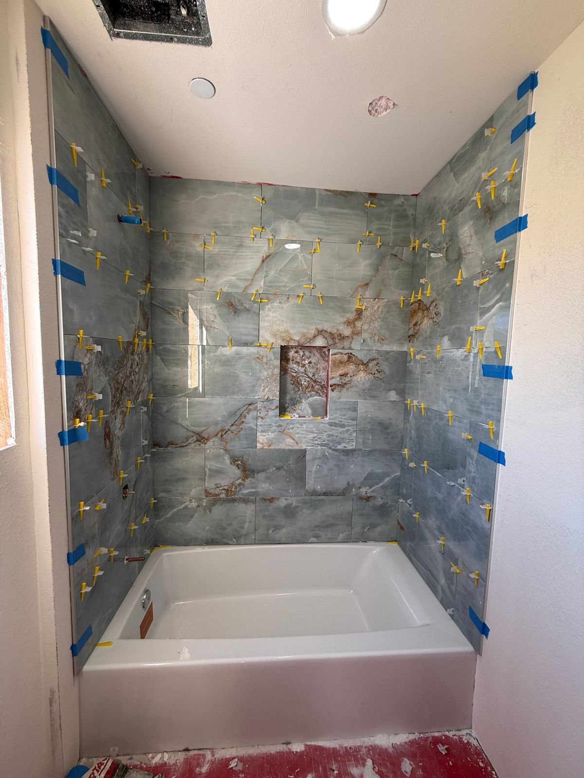 Bathtub surround with green and gold marble tile being set